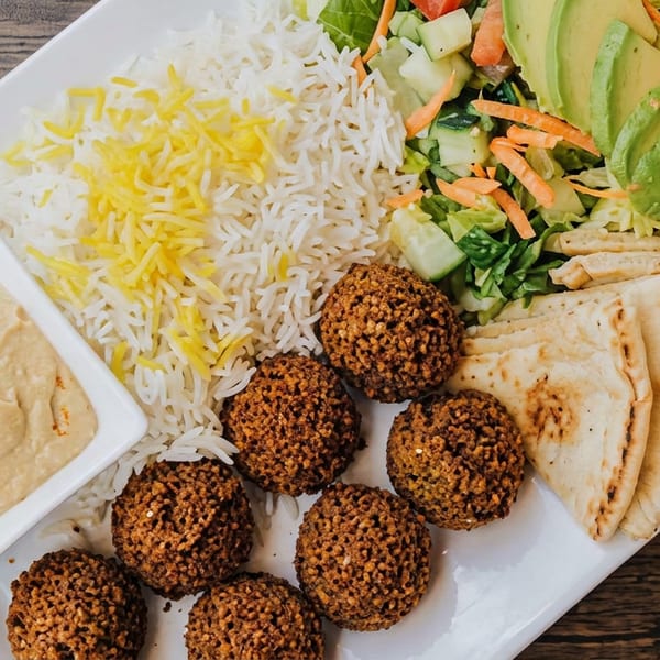 Mediterranean platter with falafel, hummus, basmati rice, pita bread, and fresh salad with avocado.
